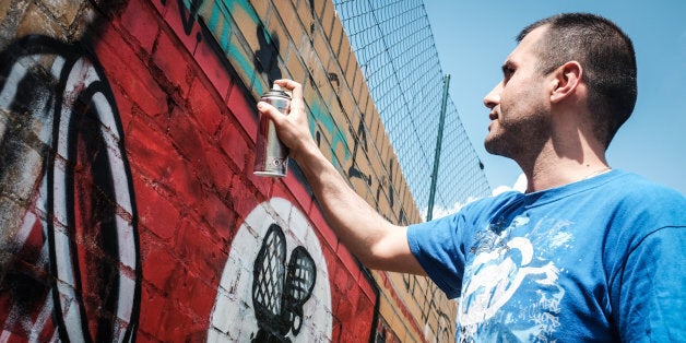 Picture taken on May 11, 2016 shows street artist Ibo Omari overpainting a swastika in Berlin.A ragtag band of Berlin street artists is taking aim at an urban scourge of neo-Nazi graffiti, using 'love and humour' to turn swastikas into colourful symbols of inclusiveness. / AFP PHOTO / dpa / Sophia Kembowski / RESTRICTED TO EDITORIAL USE - MANDATORY MENTION OF THE ARTIST UPON PUBLICATION - TO ILLUSTRATE THE EVENT AS SPECIFIED IN THE CAPTION///TO GO WITH AFP STORY BY OCEANE LAZE AND DEBORAH COLE (Photo credit should read SOPHIA KEMBOWSKI/AFP/Getty Images)