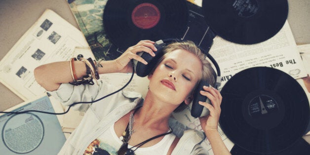 A young woman listening to music while lying on her back and surrounded by records