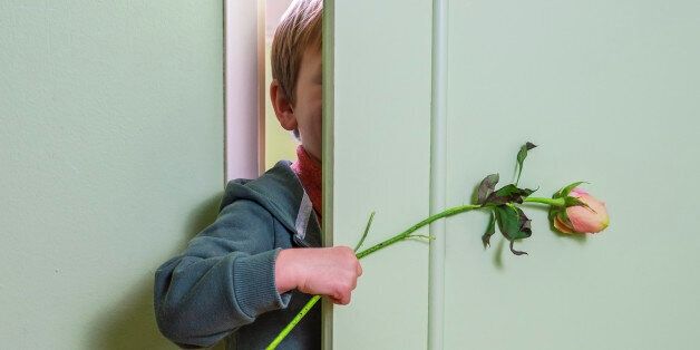 little kid hiding behind the door and holding a flower