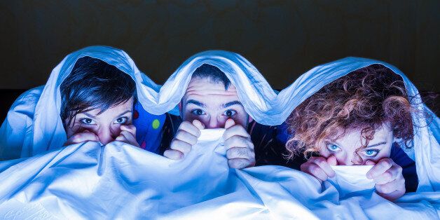 Young people watching a movie on tv under the sheets.