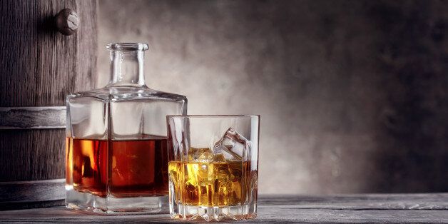 Square decanter and a glass of whiskey with ice on background barrel