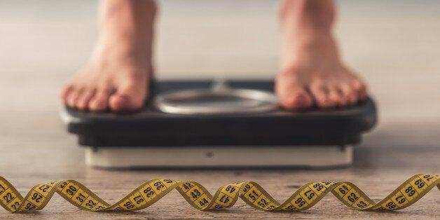 Cropped image of woman feet standing on weigh scales, on gray background. A tape measure in the foreground