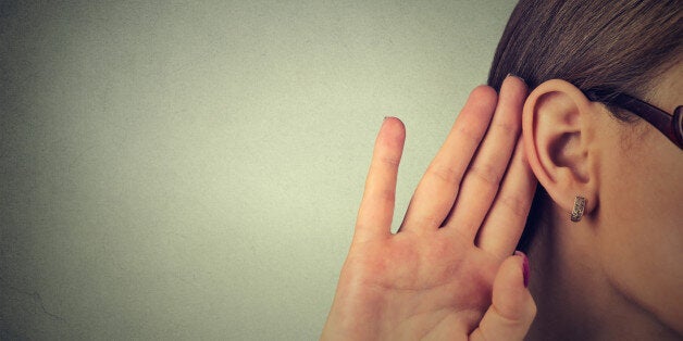 Woman holds her hand near ear and listens carefully isolated on gray wall background