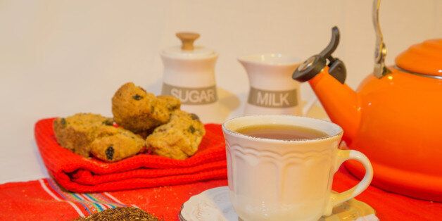 An arrangement of Rooibos tea, rusks, tea leaves with a sugar jar, milk jug and orange kettle.