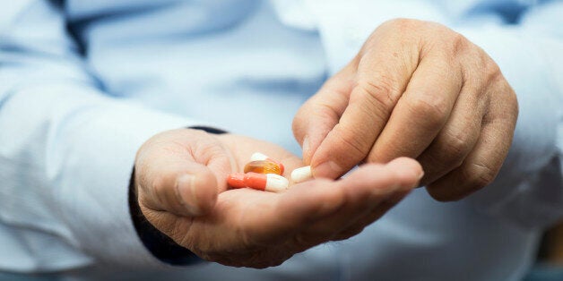 Senior man is holding yellow gel capsules in hand, horizontal