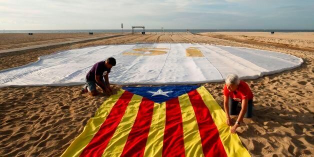 Two people unfold an 'Estelada' (Pro-independence Catalan flag) beside a banner reading 'SI' (Yes) on El Masnou beach, near Barcelona, on September 3, 2017, during an action called by ANC (Catalan National Assembly) to support a referendum on independence in Catalonia. / AFP PHOTO / Pau BARRENA CAPILLA (Photo credit should read PAU BARRENA CAPILLA/AFP/Getty Images)