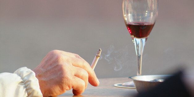 Close up of a man's hand with smoking cigarette and a glass of red wine