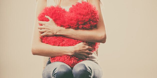 Broken heart love concept. Sad unhappy woman hugging red heart pillow