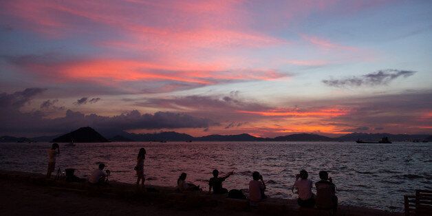 People watch as the sun sets over Victoria Harbour in Hong Kong on June 26, 2016.The official Hong Kong Observatory issued a hot weather warning on June 26 as a subtropical ridge continued to bring very hot weather to southern China. / AFP / DALE DE LA REY (Photo credit should read DALE DE LA REY/AFP/Getty Images)