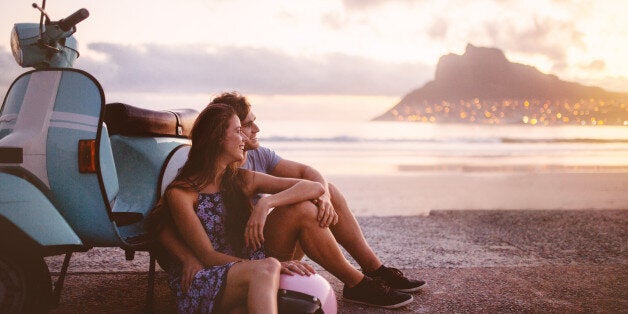 Young couple at the beach sitting next to their scooter and looking out at the sea