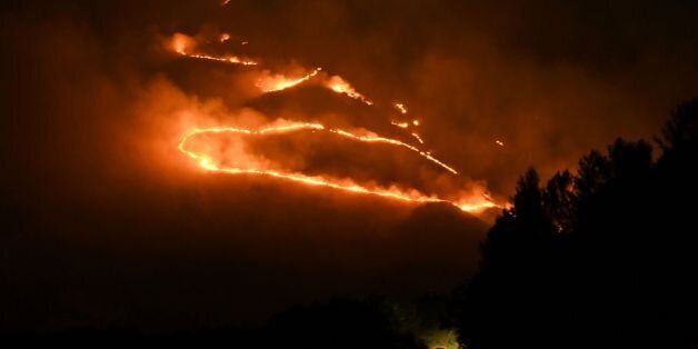 A picture taken late on August 9, 2017 shows as car driving on a road as flames and smoke rise from a forest in fire near Sarande in the Muzina mountain region, southern Albania.Forest fires have spread all over Albania, often in hardly accessible and remote areas, as the country has been engulfed by an unusual heat wave. / AFP PHOTO / Gent SHKULLAKU (Photo credit should read GENT SHKULLAKU/AFP/Getty Images)