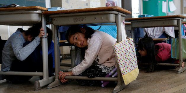 School children take shelter under desks during an earthquake simulation exercise in an annual evacuation drill at an elementary school in Tokyo, Japan March 10, 2017, a day before the six-year anniversary of the March 11, 2011 earthquake and tsunami disaster that killed thousands and set off a nuclear crisis. REUTERS/Issei Kato