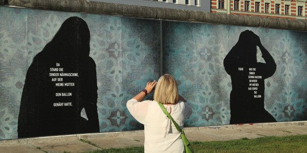 BERLIN, GERMANY - AUGUST 14: A visitor photographs a portion of the art installation 'Beyond The Wall' by German-American artist Stefan Roloff at a section of the former Berlin Wall called the East Side Gallery on August 14, 2017 in Berlin, Germany. The installation, which will be up from August 13 through November 9, combines images from the Berlin Wall during the Cold War with the accounts of people persecuted by the East German secret police. (Photo by Sean Gallup/Getty Images)