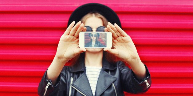 Fashion woman makes self portrait on smartphone over city pink background