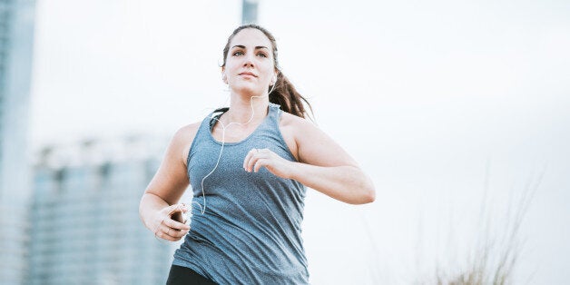 A young adult woman goes for a morning run, crossing the Lamar Street pedestrian bridge in Austin, Texas. The bridge gets a large volume of foot traffic in the morning with people exercising at the start of their day. She has a focused look of determination, listening to music on her smartphone.