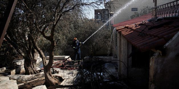 A firefighter drops water on a burnt-out house following a wildfire in the area of Kalyvia, near Athens, Greece August 3, 2017. REUTERS/Alkis Konstantinidis