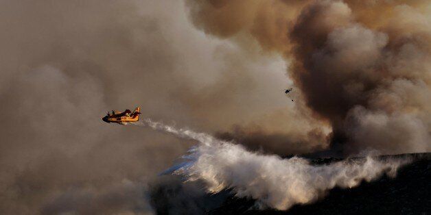 TOPSHOT - A Canadair firefighting airplane drops water above a fire at sunset, east of Athens on August 15, 2017.The army was called in to assist firefighters around Kalamos, 45 kilometres (30 miles) east of Athens, where a fire has been burning since August 13. In all, 146 fires have broken out across Greece since then according to authorities. / AFP PHOTO / ARIS MESSINIS (Photo credit should read ARIS MESSINIS/AFP/Getty Images)