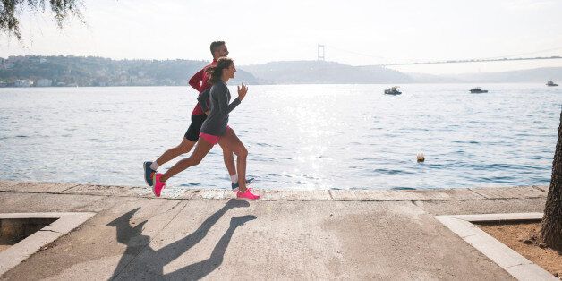 Active energetic couple running together outdoors at the waterfront.