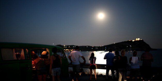 People watch the full moon rising over the sky of Sounio, some 60 kilometers south of Athens on August 10 2014. AFP PHOTO / Angelos Tzortzinis (Photo credit should read ANGELOS TZORTZINIS/AFP/Getty Images)