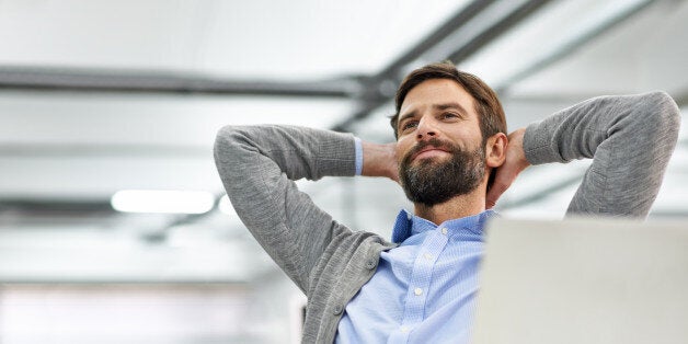 Shot of a young businessman working on his laptop in the office and leaning back in his chair