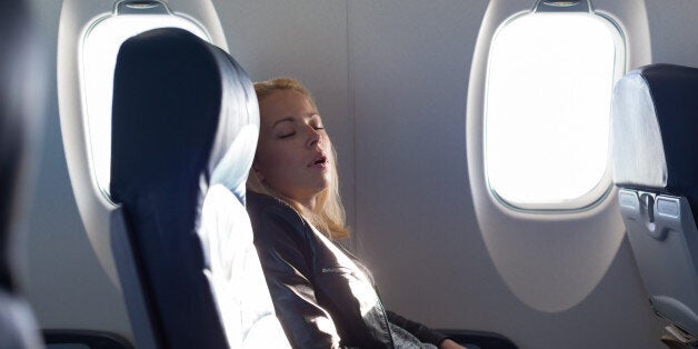 Tired blonde casual caucasian lady napping on uncomfortable seat while traveling by airplane. Commercial transportation by planes.