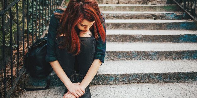 Depressed young woman sitting on stairs outdoors, with copy space