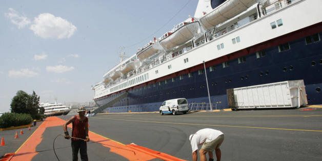 ATHENS, GREECE: Workers are seen painting an Olympic lane along the 'Ocean Countess' cruiseship that is docked at the Peiraias main port, near Athens City, 03 August 2004. The cruiseship arrived in the port to host some of members of the Olympic family, VIP, and the media. AFP PHOTO / Fayez NURELDINE (Photo credit should read FAYEZ NURELDINE/AFP/Getty Images)