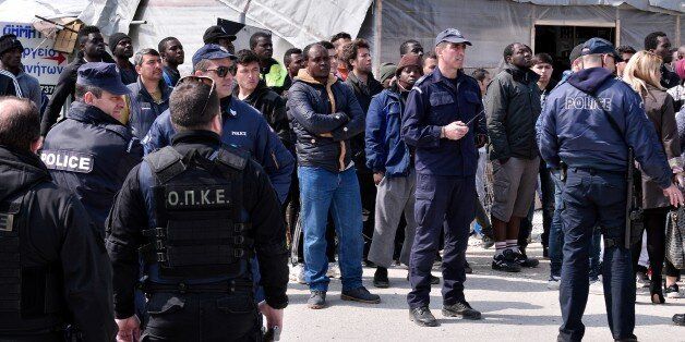 A picture taken on March 16, 2017 shows policemen standing guard near migrants at the Moria migrant camp on the island of Lesbos, almost a year after an EU-Turkey deal. The deal, signed on March 18, 2016, has sought to stem the flow of migrants from Turkey to the EU, in particular Greece, by land and sea routes.Some 3000 refugees and migrnts live in the Moria camp , out of some 14000 stucked on the Aegean islands since the closing of the borderss and the implementation of the deal. / AFP PHOTO / LOUISA GOULIAMAKI (Photo credit should read LOUISA GOULIAMAKI/AFP/Getty Images)