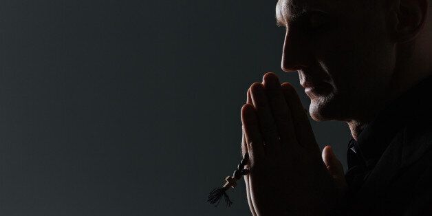 Silhouette of man holding rosary and praying over black background