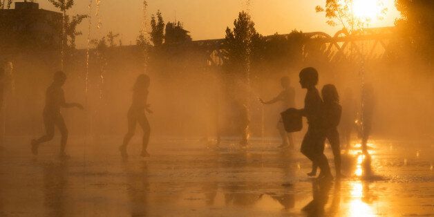 Madrid, Spain - July 12, 2013: Young kids scape from the summer heat wave at dusk playing with the water jets in the fountains of the recently renovated Madrid RA-o park, by the Manzanares River in Madrid, Spain.