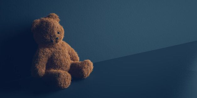 Teddy bear with torn eye sits in dark room. Child abuse and violence concept.