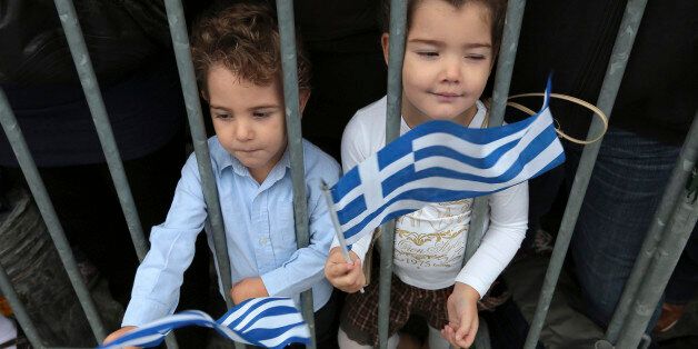 Children wave Greek flags as they watch a student parade marking the anniversary of
