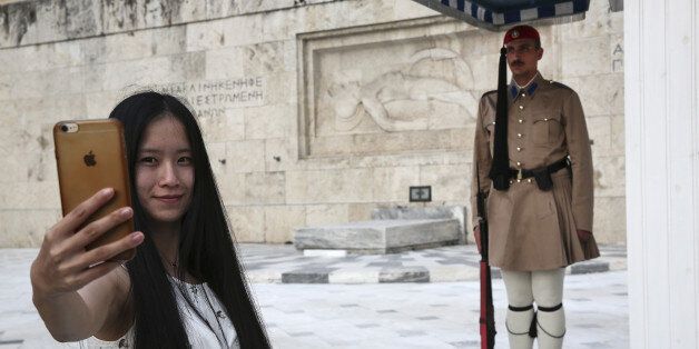 A Chinese tourist takes a photograph of a presidential at the Tomb of the Unknown Soldier on Syntagma Square in Athens, Greece, on Wednesday, May 24, 2017. Fosun International Ltd., the Chinese conglomerate thats part of a venture to transform the former Athens airport site into one of the biggest real-estate projects in Europe, is now turning its attention to Greek tourism. Photographer: Yorgos Karahalis/Bloomberg via Getty Images