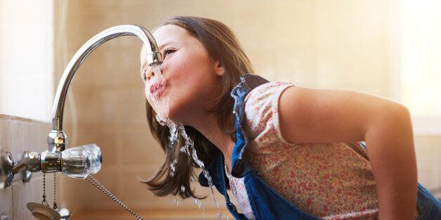 Shot of a little girl drinking water directly from the kitchen tap at home