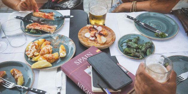 Tourists in Barcelona eating tapas in a typical restaurant in the Barri Gotic. On the table a travel guide of Spain and a smartphone.
