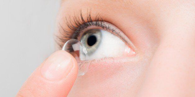 Woman inserting a contact lens in her eye.