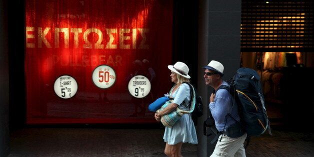 Tourists walk past a shop announcing sales in a main commercial street in central Athens, Greece July 17, 2015. A senior Greek official confirmed on Thursday that banks would reopen on Monday and said the government was looking into allowing people to bunch 60 euro withdrawals over several days. REUTERS/Yiannis Kourtoglou