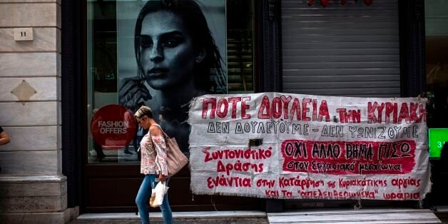 A woman walks past a banner that reads ''No work on Sunday'' during a protest against the opening of shops 30 Sundays per year, a condition under Greece's bailout on May 7, 2017. / AFP PHOTO / Angelos Tzortzinis (Photo credit should read ANGELOS TZORTZINIS/AFP/Getty Images)