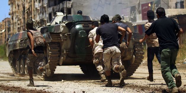 Members of the Libyan National Army (LNA), also known as the forces loyal to Marshal Khalifa Haftar, take cover behind an armoured vehicle during clashes against jihadists in Benghazi's Al-Hout market area on May 20, 2017. / AFP PHOTO / Abdullah DOMA (Photo credit should read ABDULLAH DOMA/AFP/Getty Images)