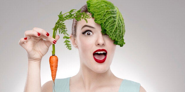 Portrait of a woman illustrating a vegan concept holding a carrots and with a cabbage on the head