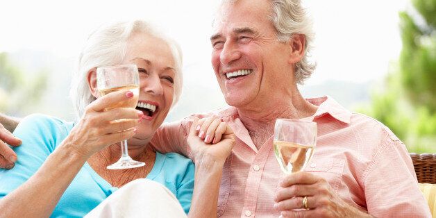 Senior Couple Sitting On Outdoor Seat Together Drinking Wine Laughing