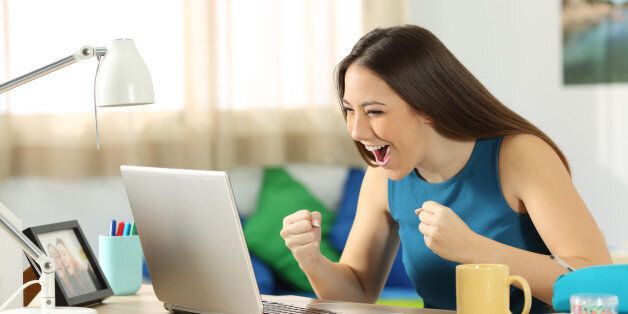 Single excited student on line with a laptop sitting in a desk in her room in a house interior