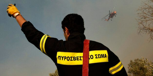 A firefighter gestures as a fire-fighting helicopter flies in the background during a forest fire at Domvrena village, about 120km (75 miles) north of Athens, August 17, 2009. A forest fire raged out of control in central Greece on Monday, burning isolated farm houses and olive groves and threatening villages, local authorities said. REUTERS/Yiorgos Karahalis (GREECE DISASTER ENVIRONMENT)