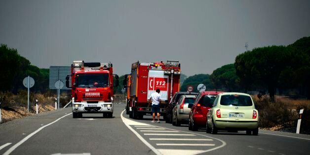 Firefighter vehicles block a road after a wildfire in Mazagon, on July 25, 2017.More than 1,500 people were evacuated as a precaution on June 25, 2017 after a fire broke out at a nature reserve in southern Spain famed for its biodiversity.The fire started overnight and had by morning encroached on the Donana National Park at Moguer in the southern region of Andalusia, Jose Fiscal, deputy head of the regional environment protection authority, told Spanish television. / AFP PHOTO / CRISTINA QUICLE