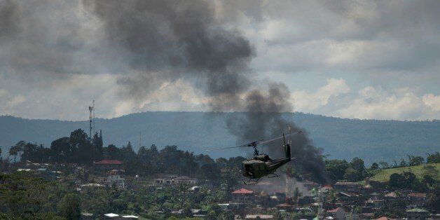 A helicopter flies through smoke billowing from houses after aerial bombings by Philippine Airforce planes on Islamist militant positions in Marawi on the southern island of Mindanao on June 17, 2017.Philippine troops pounded Islamist militants holding parts of southern Marawi city with air strikes and artillery on June 17 as more soldiers were deployed and the death toll rose to more than 300 after nearly a month of fighting. / AFP PHOTO / Noel CELIS (Photo credit should read NOEL CELIS/
