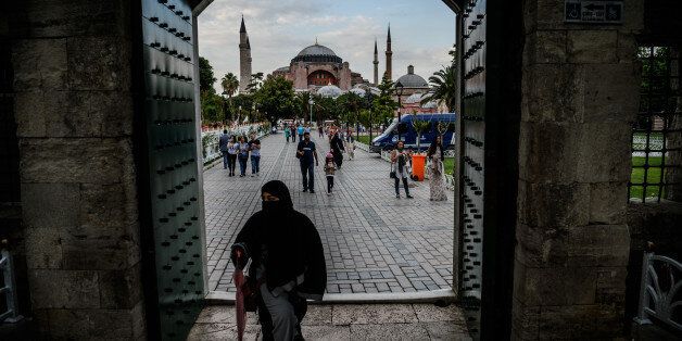 TOPSHOT - A woman walks through a gate of the Blue mosque square before breaking time as Hagia Sofia is seen on the background on June 6, 2016 in Istanbul, during the first day of the holy month of Ramadan. More than a billion Muslims observed the start of Ramadan on May 6 but in the besieged cities of Syria and Iraq residents struggled to mark the holy month. Marking the divine revelation received by Prophet Mohammed, the month sees Muslim faithful abstain from eating, drinking, smoking and having sex from dawn to dusk. They break the fast with a meal known as iftar and before dawn have a second opportunity to eat and drink during suhur. The month is followed by the Eid al-Fitr festival. / AFP / OZAN KOSE (Photo credit should read OZAN KOSE/AFP/Getty Images)
