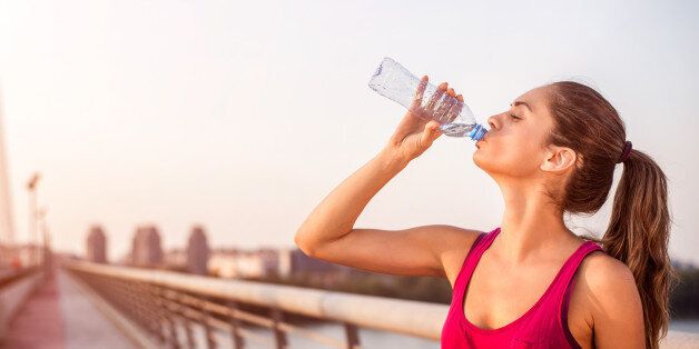 Young sportswoman with pony tail drinking water on the bridge while resting from morning jogging.