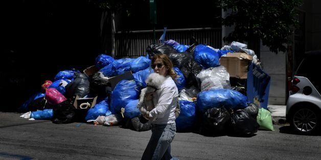 TOPSHOT - A woman holding her dog walks past a pile of garbage in central Athens on June 22, 2017, as contract garbage collectors refuse for the third day to pick up garbage cans and demand the renewal of their contracts. / AFP PHOTO / ARIS MESSINIS (Photo credit should read ARIS MESSINIS/AFP/Getty Images)