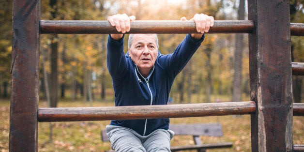 The photo of a senior man exercising. He wears blue sweatshirt and grey sweatpants. He is in shape of his life.