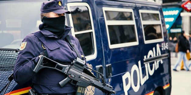 Madrid, Spain - February 2, 2015: Madrid policeman armed with machine gun and hand gun at Puerta del Sol in centre of Madrid. Behind him a police car with large letters saying POLICE